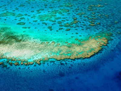 An aerial photo of turquoise and darker blue water around an area of the Great Barrier Reef. 